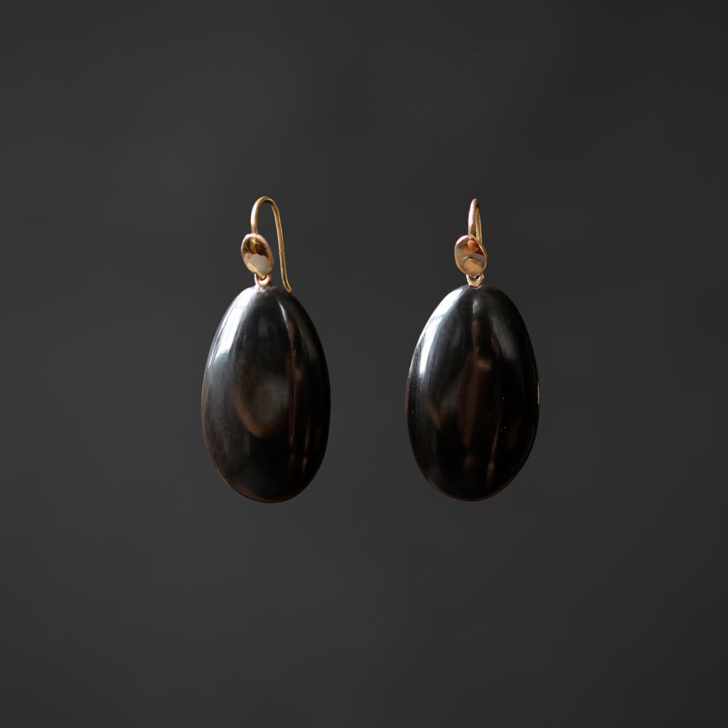 A pair of dangling earrings with polished black teardrop-shaped pendants and gold-tone hooks, shown against a dark gray background.