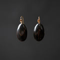 A pair of dangling earrings with polished black teardrop-shaped pendants and gold-tone hooks, shown against a dark gray background.