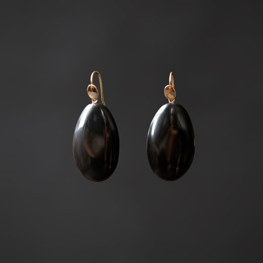 A pair of dangling earrings with polished black teardrop-shaped pendants and gold-tone hooks, shown against a dark gray background.