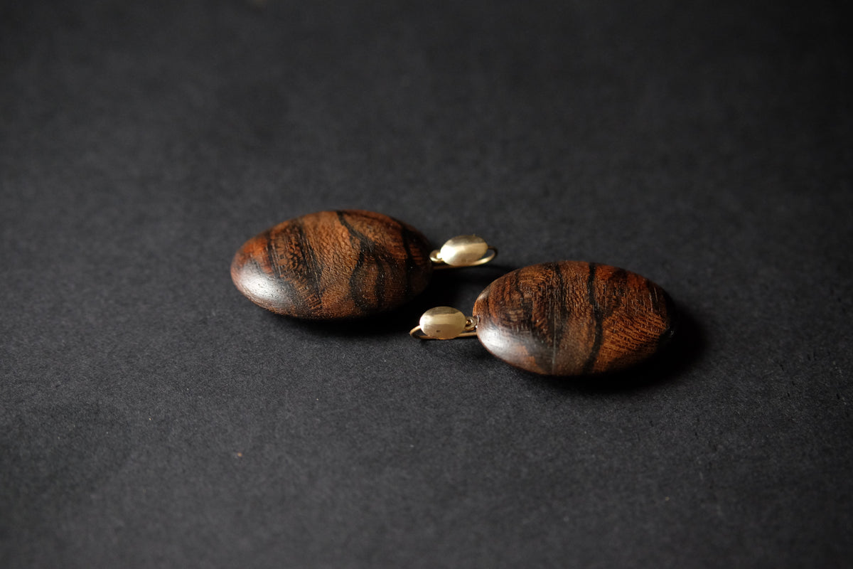 A pair of handmade drop earrings made from polished dark brown wood beads with natural grain patterns, connected by small gold-colored metal spacers, set against a dark textured background.