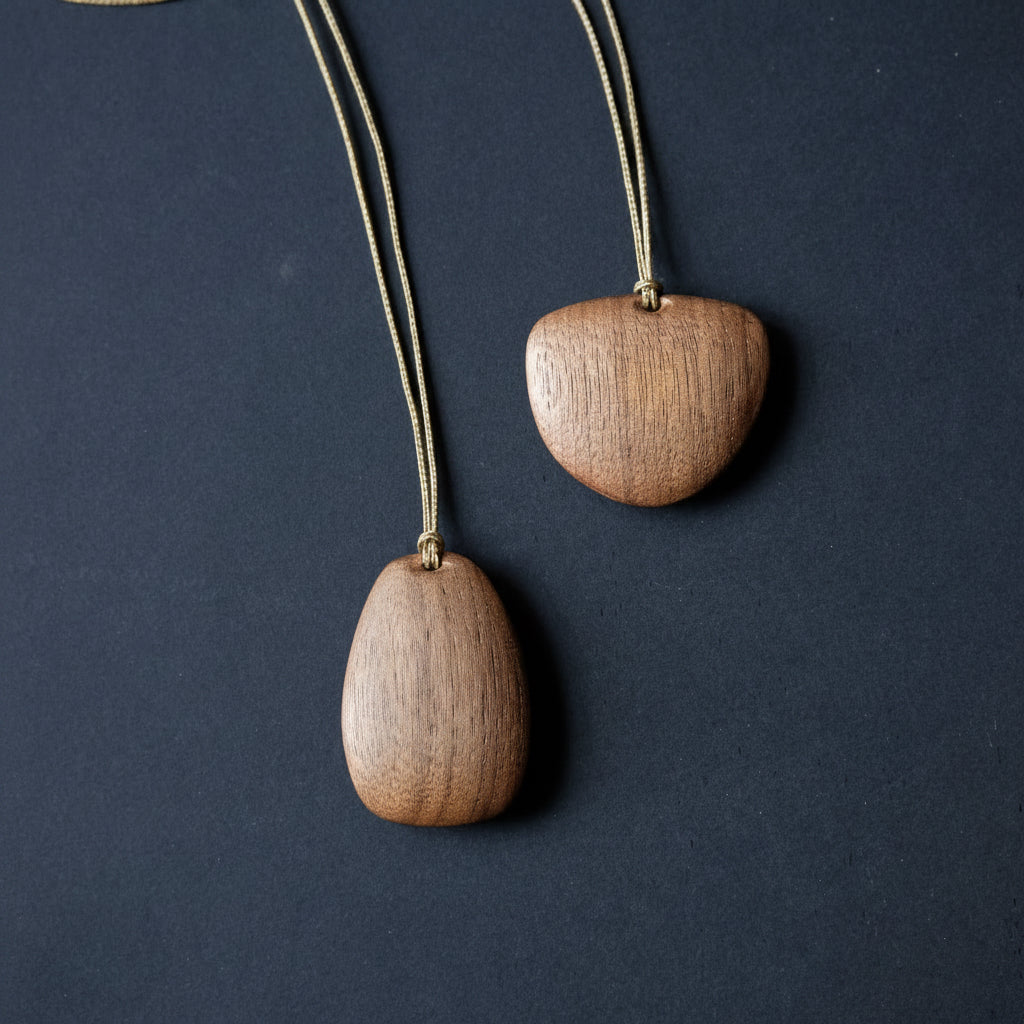 Two wooden pendant necklaces with smooth teardrop-shaped wood pendants on thin cords, displayed against a dark textured background.
