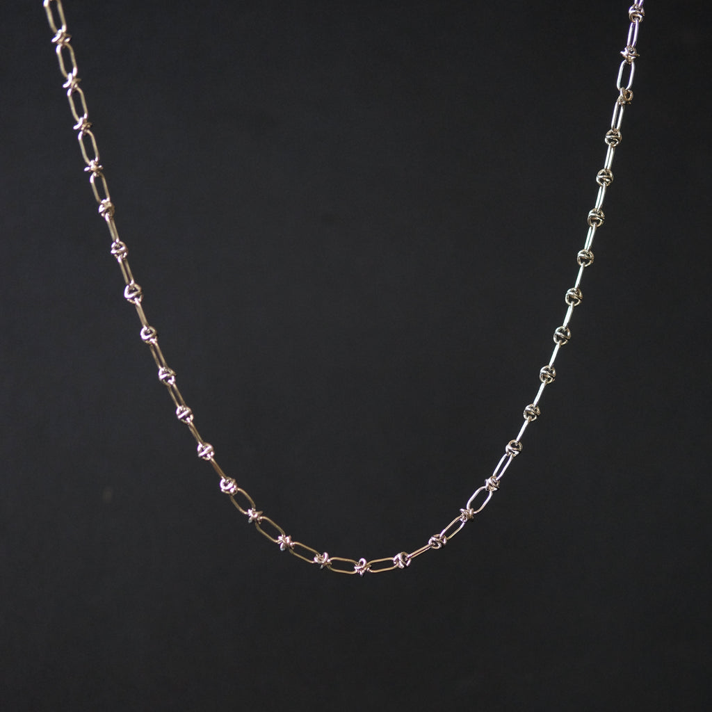 A delicate chain necklace with alternating elongated oval links and small star-shaped links, shown against a solid black background.
