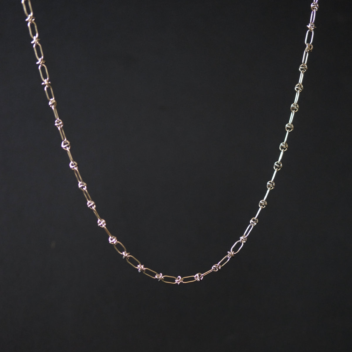 A delicate chain necklace with alternating elongated oval links and small star-shaped links, shown against a solid black background.