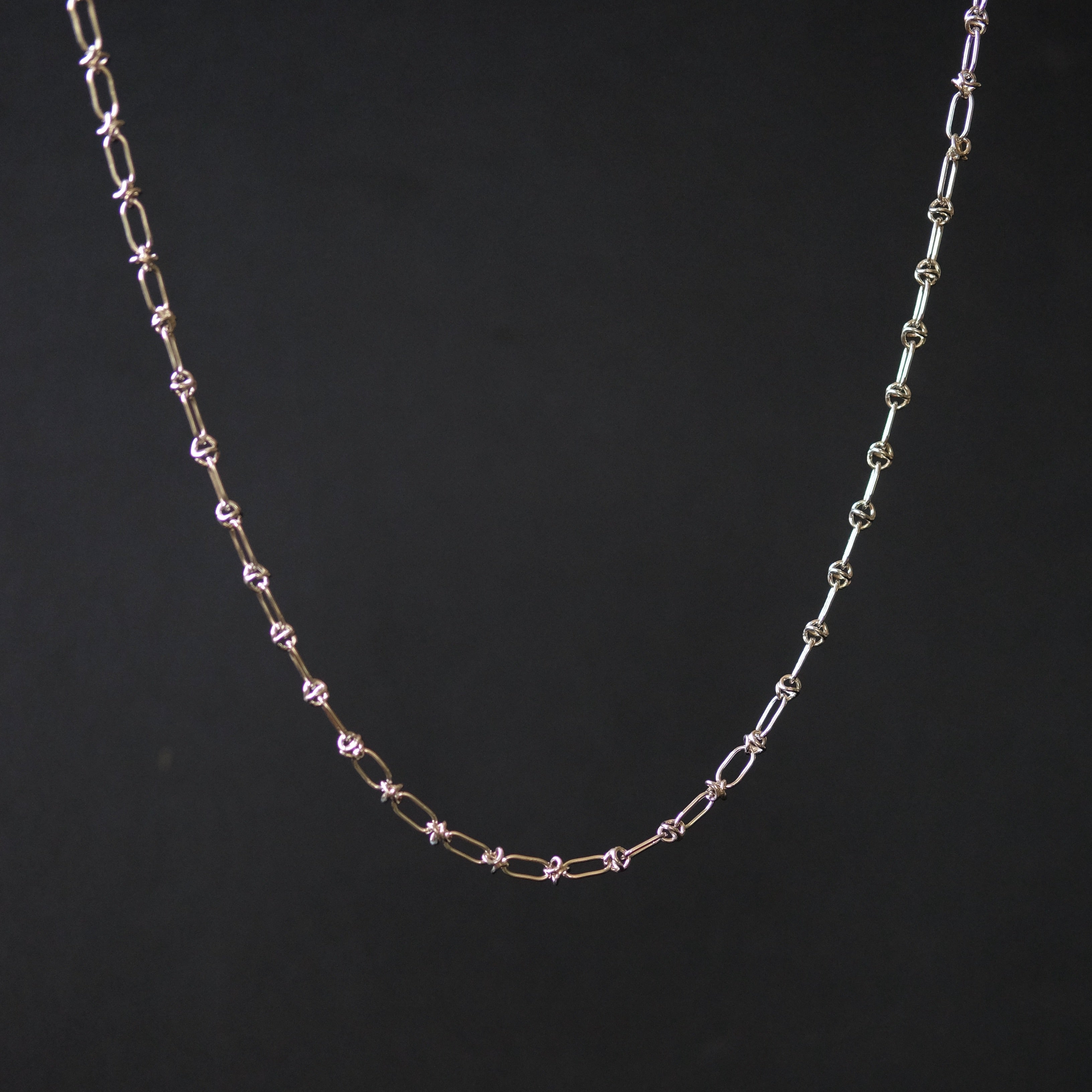 A delicate chain necklace with alternating elongated oval links and small star-shaped links, shown against a solid black background.