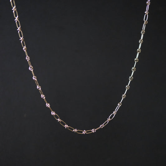 A delicate chain necklace with alternating elongated oval links and small star-shaped links, shown against a solid black background.