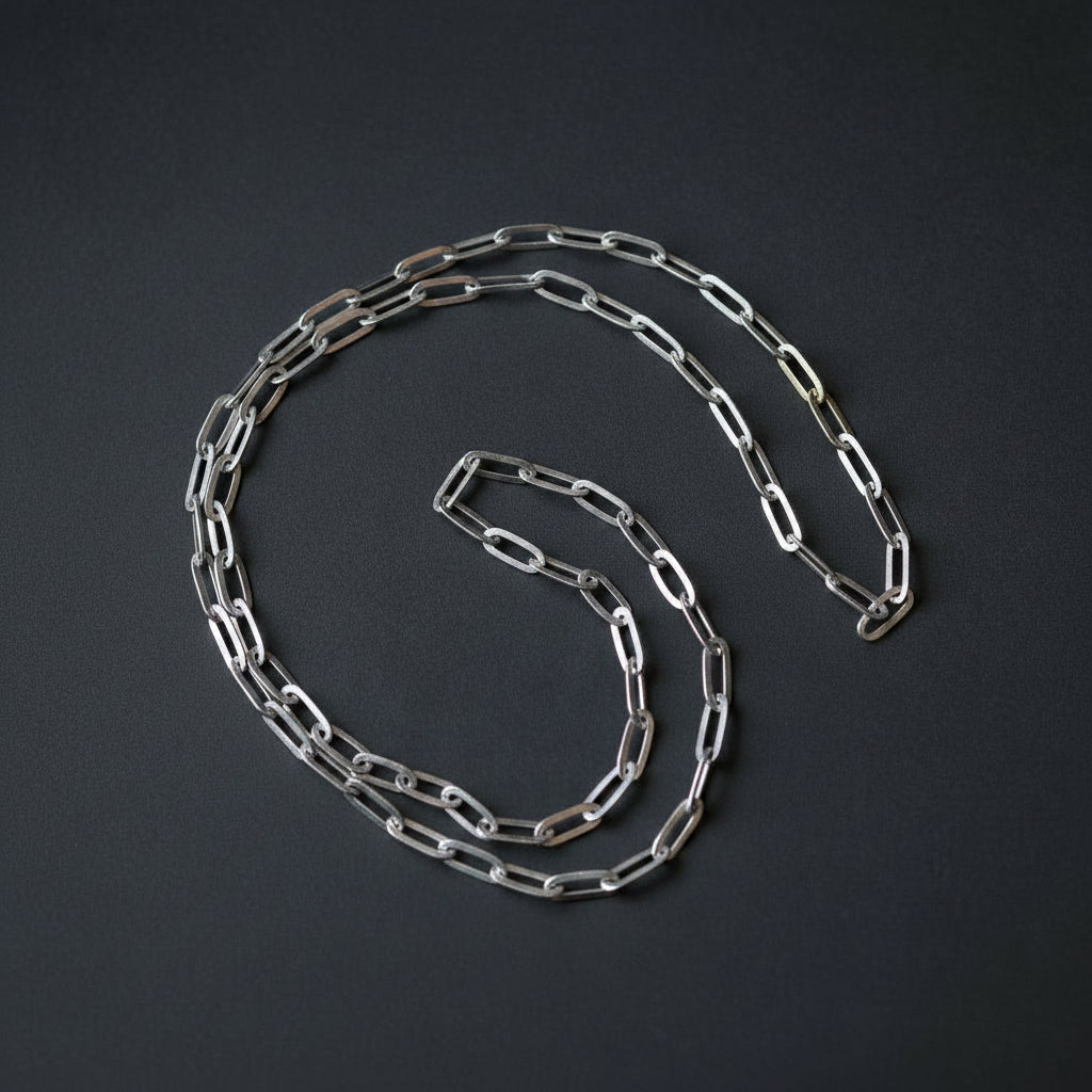 A silver paperclip chain necklace coiled on a dark gray background.