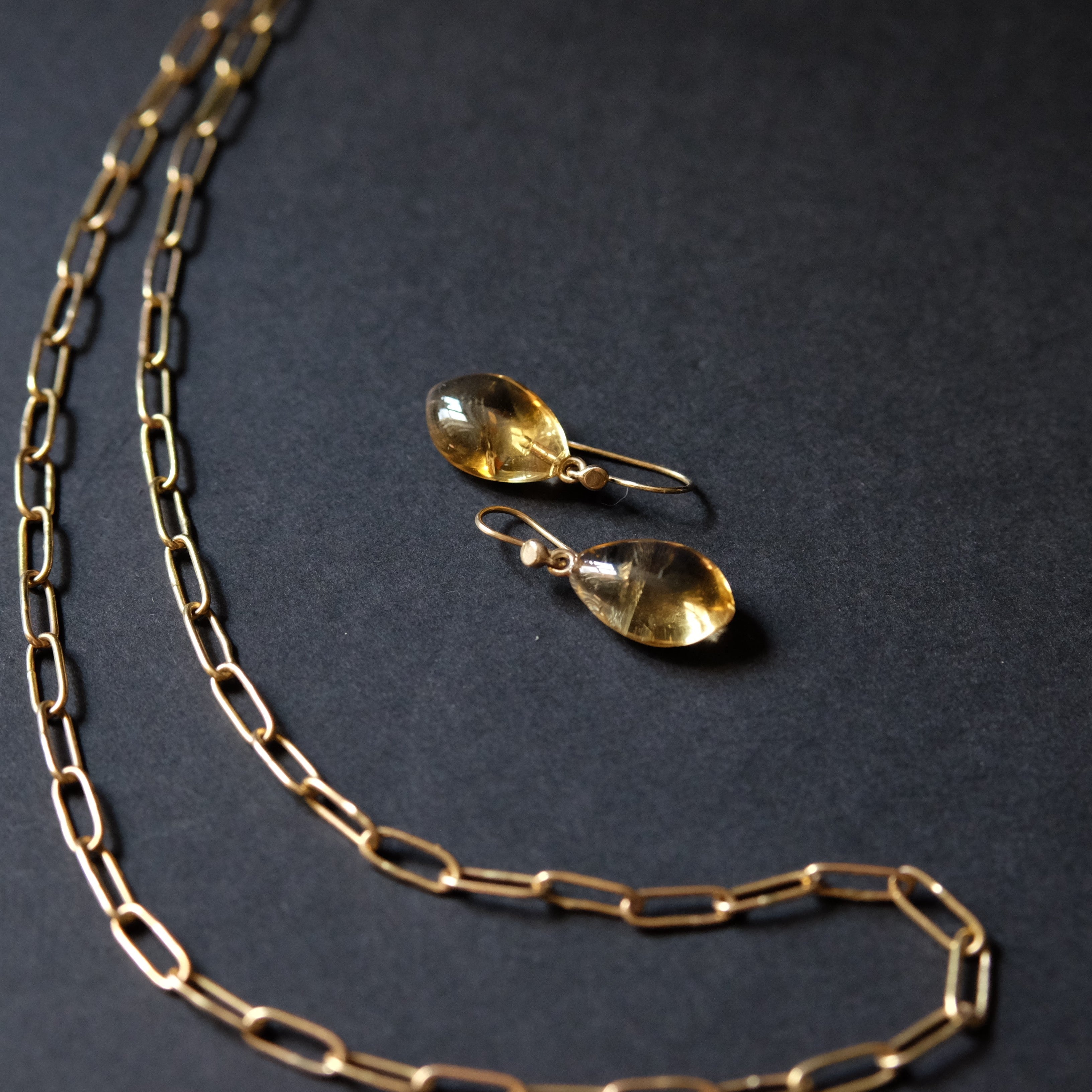 A gold chain necklace and matching drop earrings with teardrop-shaped clear gemstones, arranged on a dark textured background.