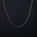 A delicate gold paperclip chain necklace draped in a U-shape against a dark textured background.