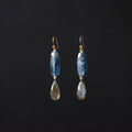 A pair of drop earrings featuring a polished blue stone bead and a teardrop-shaped labradorite stone, suspended from gold-toned hooks against a solid black background.