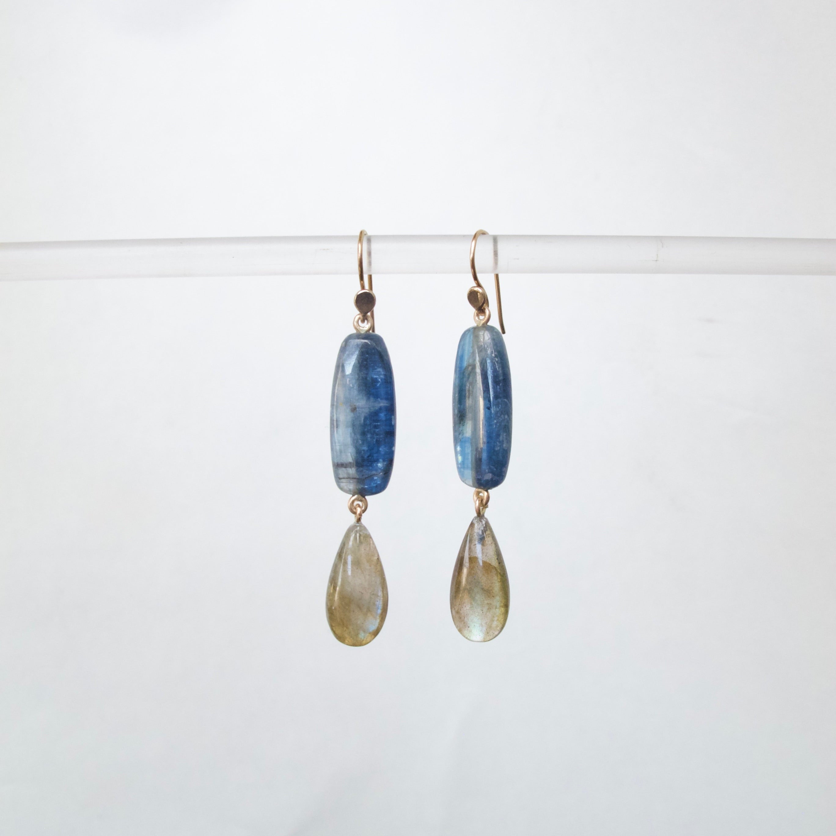 A pair of handmade dangle earrings featuring polished blue kyanite rectangular beads and teardrop-shaped smoky gray labradorite stones, suspended from gold-toned French hooks against a clean white background.