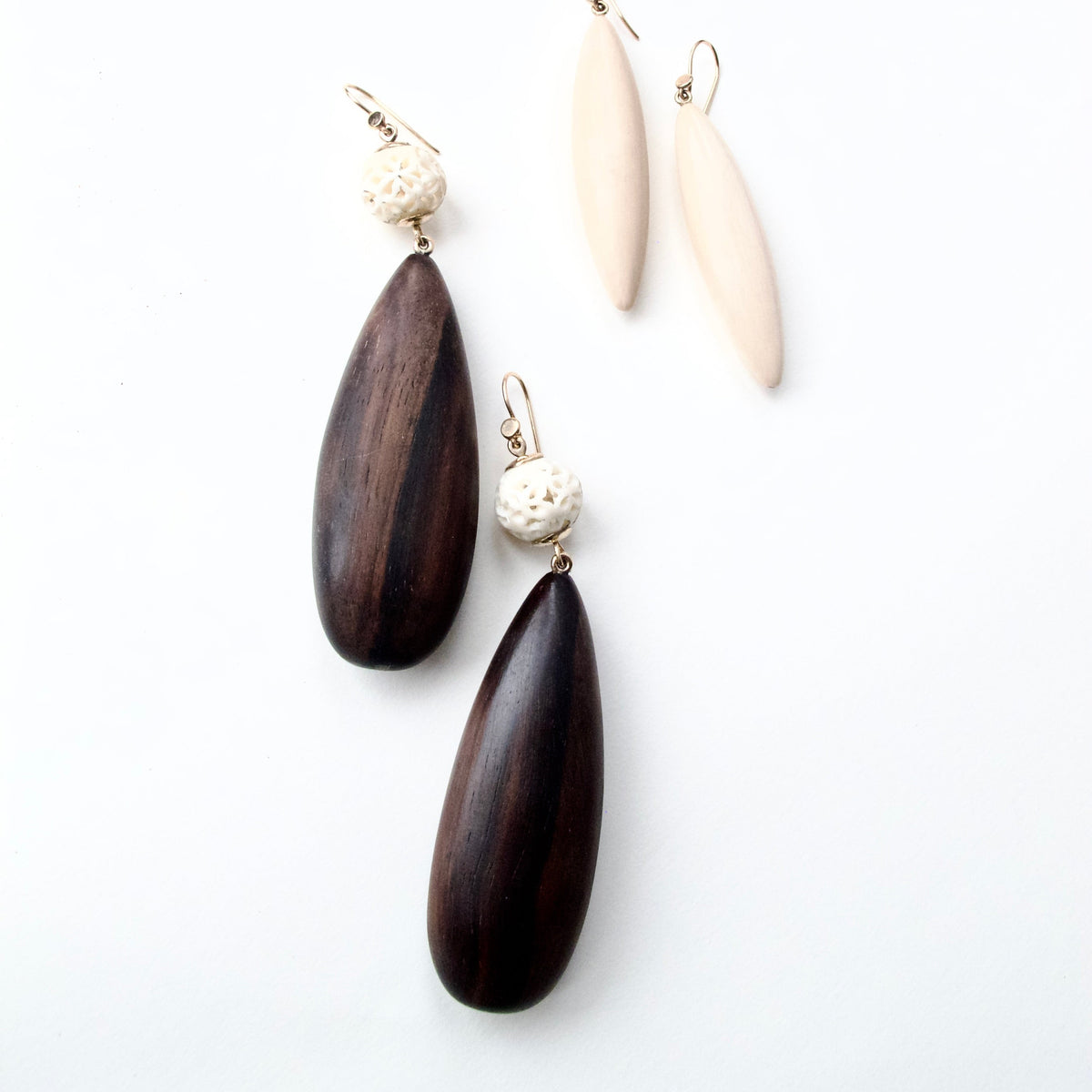 A pair of dark brown wooden teardrop dangle earrings with textured cream beads and gold-tone hooks, displayed next to a pair of matching light beige wooden teardrop earrings on a clean white background.