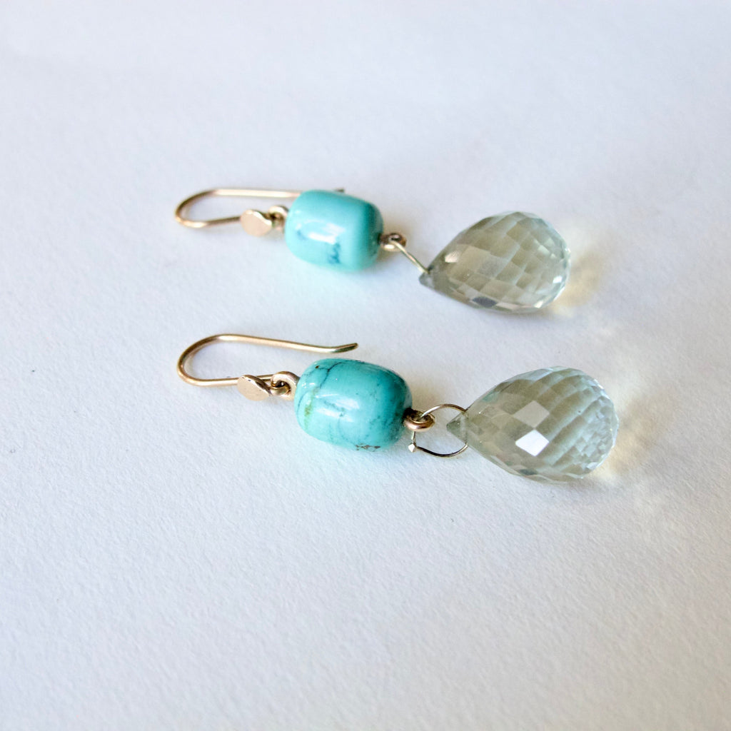 A pair of gold-tone dangle earrings featuring a round turquoise bead and a faceted clear teardrop gemstone, displayed on a clean white background.