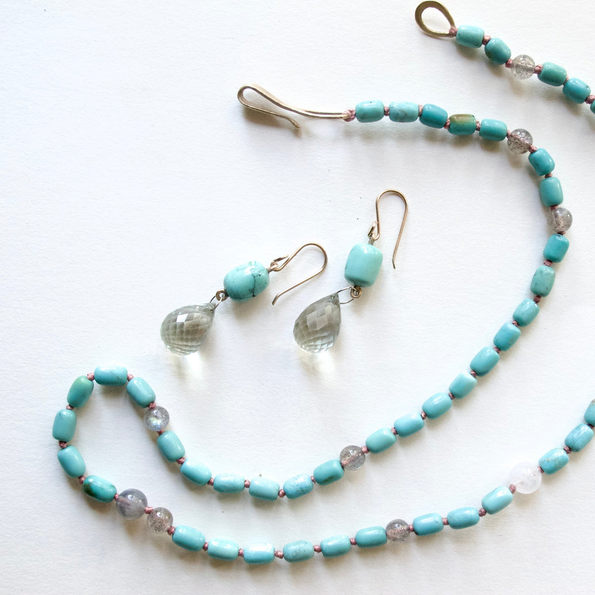 A jewelry set featuring a beaded necklace and matching drop earrings on a plain white background. The beads are a light turquoise blue, accented with small clear faceted beads and set in a gold-tone metal.