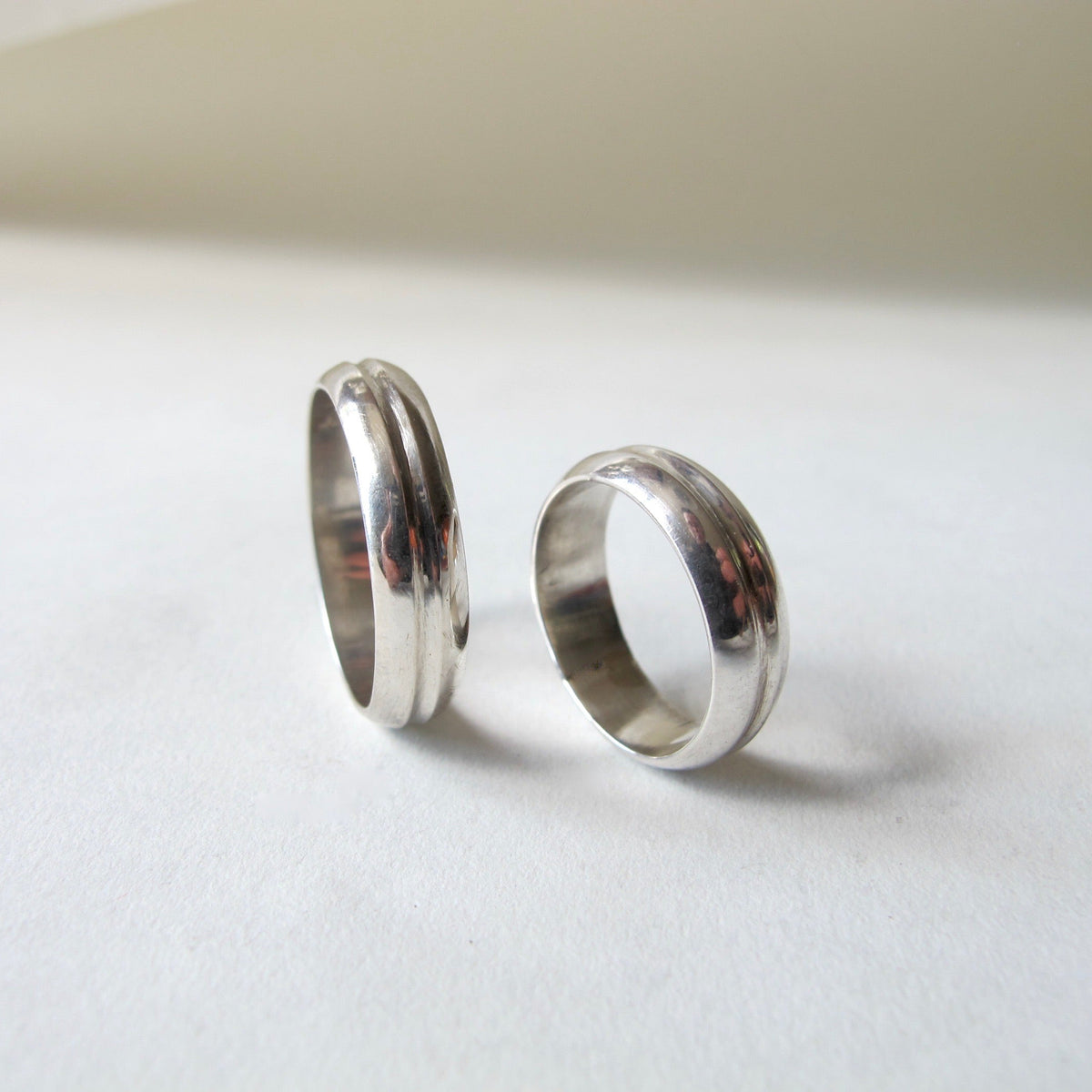 Two polished silver rings standing upright on a white surface with a soft beige background.