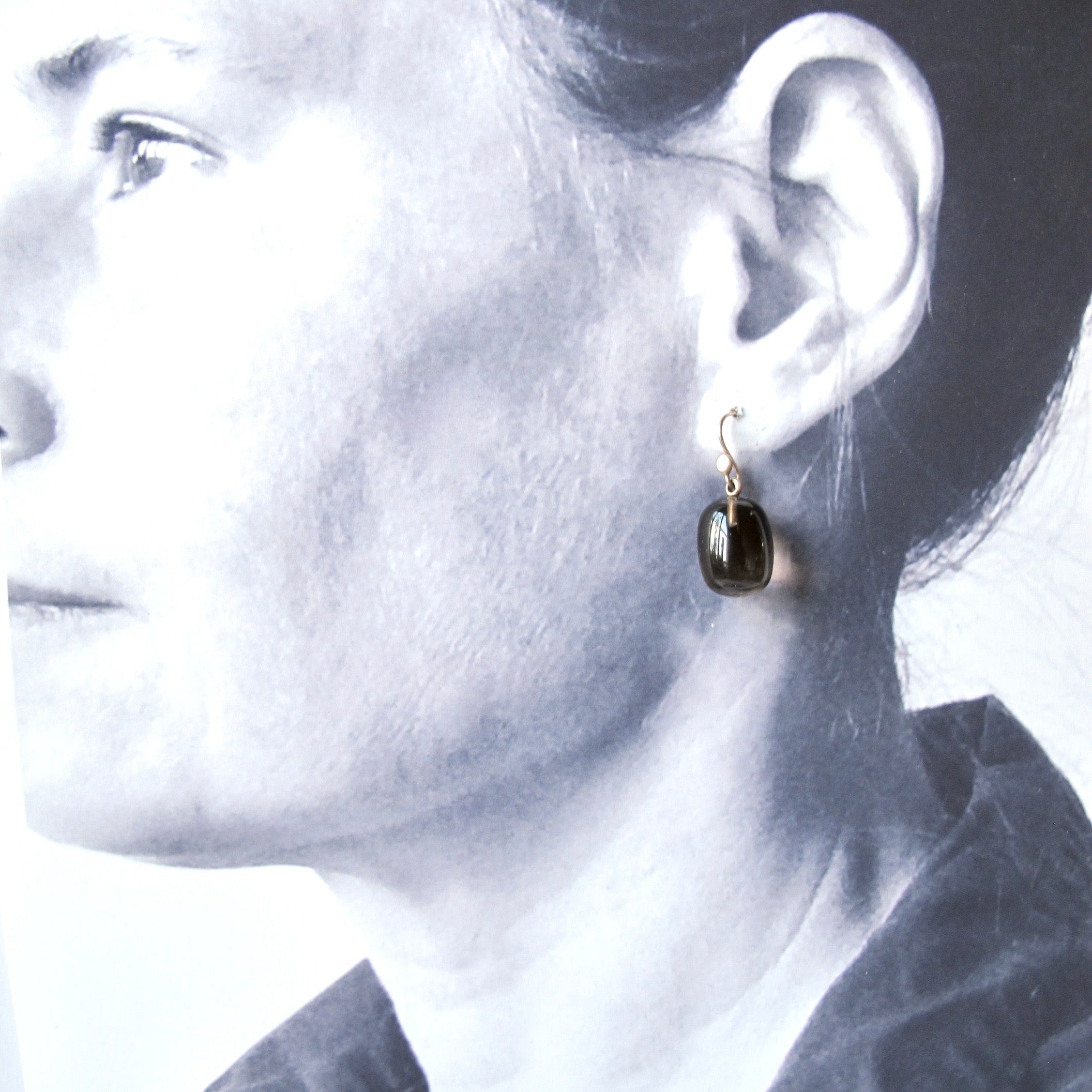A close-up side profile of a woman wearing a small gold hoop earring with a dark, polished oval stone.