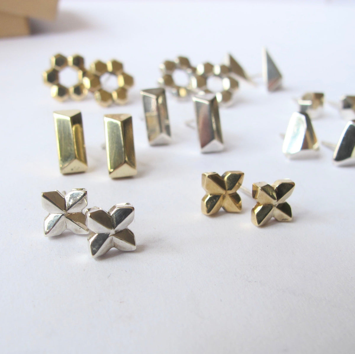 A collection of geometric stud earrings in both gold and silver finishes, arranged on a plain white surface.