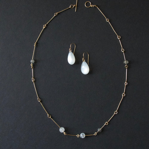 A gold-toned beaded necklace and matching drop earrings with white teardrop beads, arranged on a dark charcoal background.