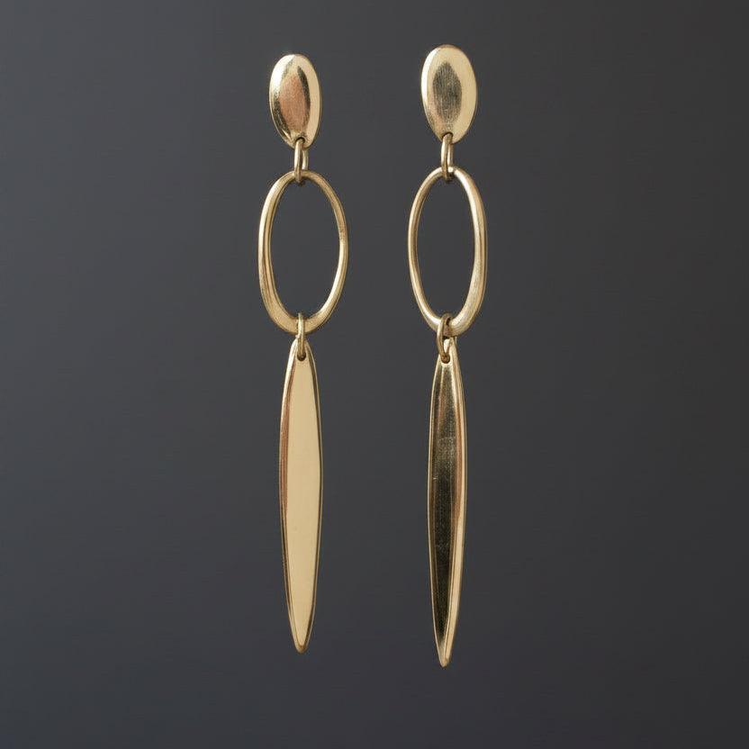 A pair of gold-toned geometric dangle earrings hanging from a clear display bar against a light gray background.
