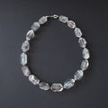 A beaded necklace made of faceted clear crystal beads with a silver clasp, displayed on a dark gray background.