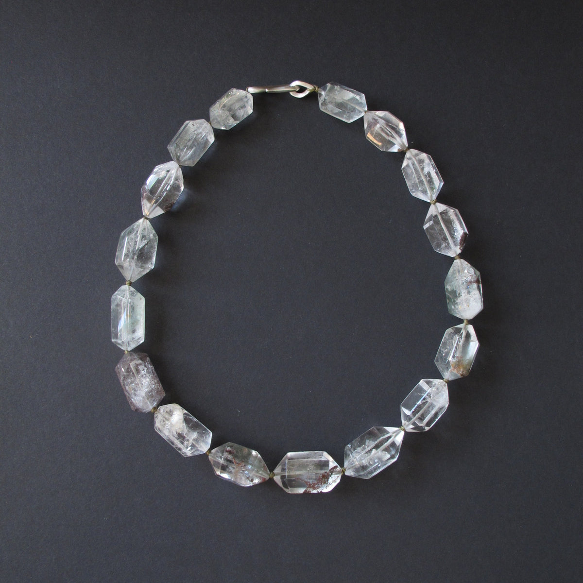 A beaded necklace made of faceted clear crystal beads with a silver clasp, displayed on a dark gray background.