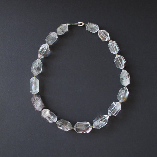 A beaded necklace made of faceted clear crystal beads with a silver clasp, displayed on a dark gray background.