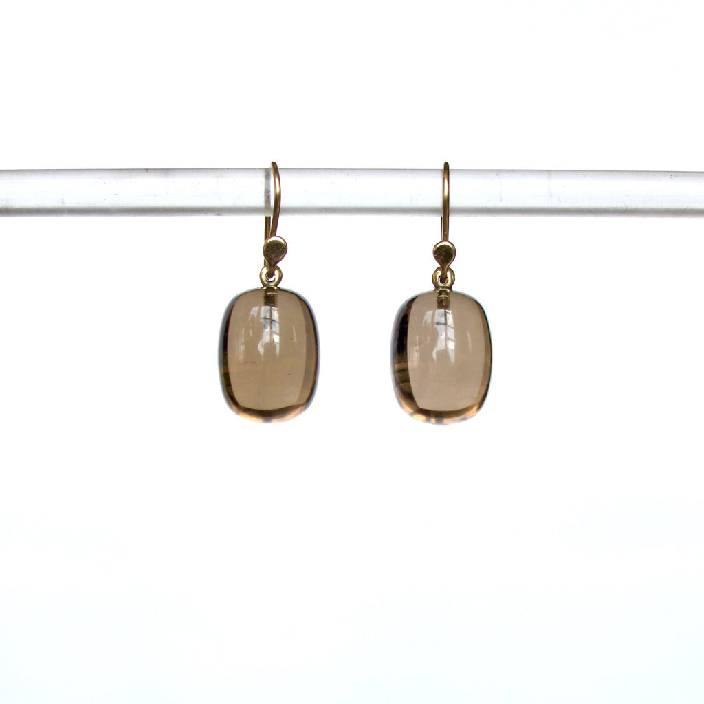 A pair of gold-tone dangle earrings with smooth, rounded translucent smoky brown gemstones, hanging from a clear horizontal display bar against a bright white background.