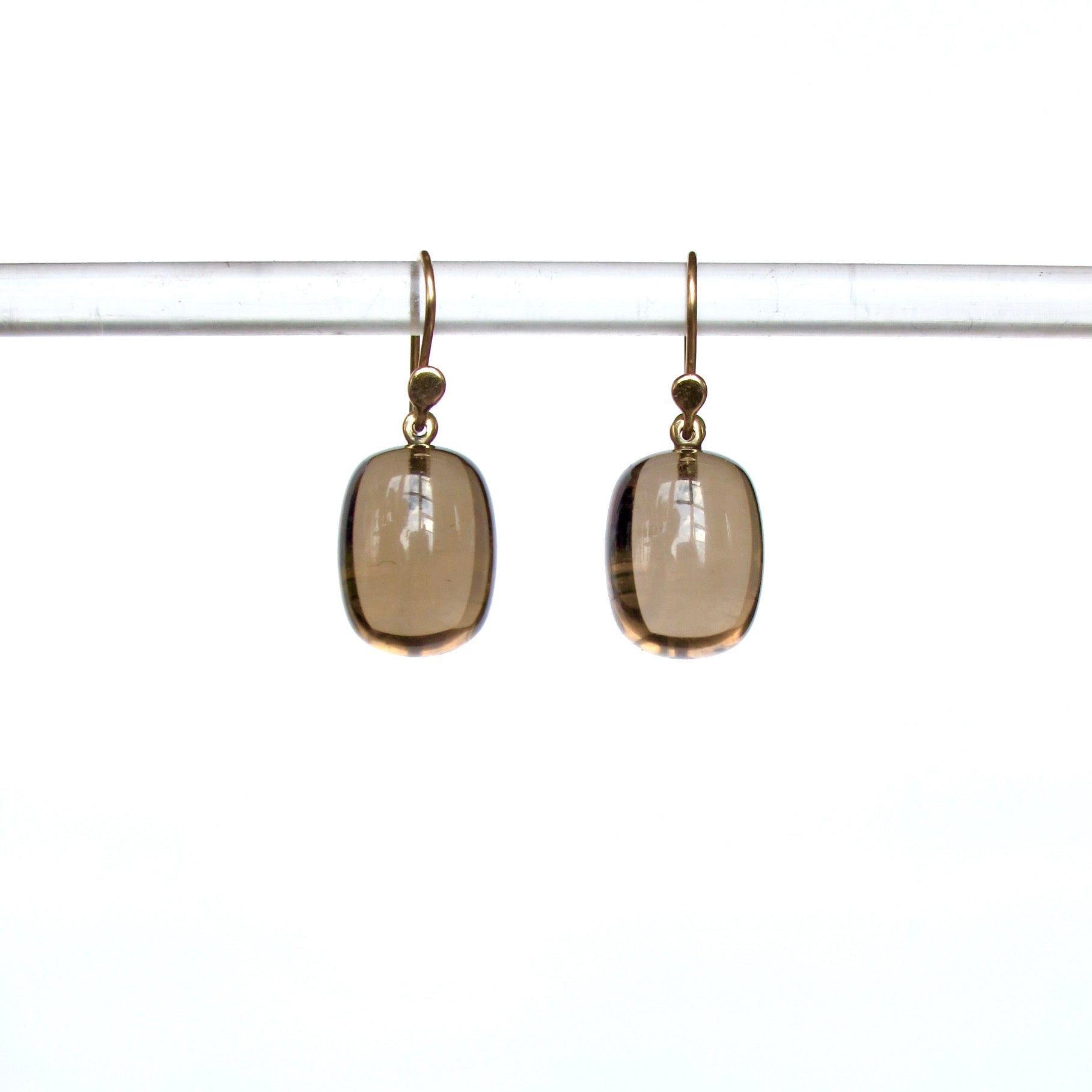 A pair of gold-tone dangle earrings with smooth, rounded translucent smoky brown gemstones, hanging from a clear horizontal display bar against a bright white background.