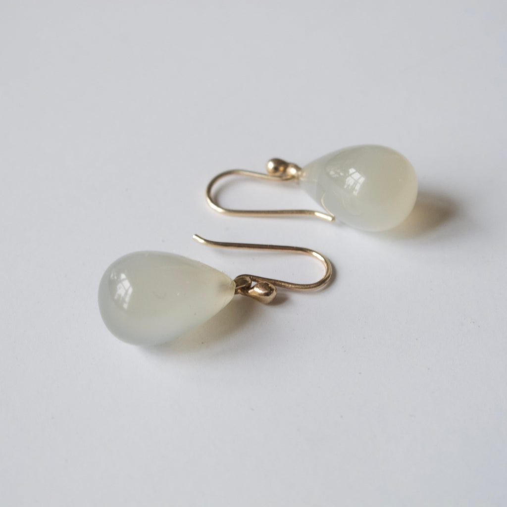A pair of gold-tone dangle earrings with teardrop-shaped, milky translucent white stone drops, displayed on a clean white background.