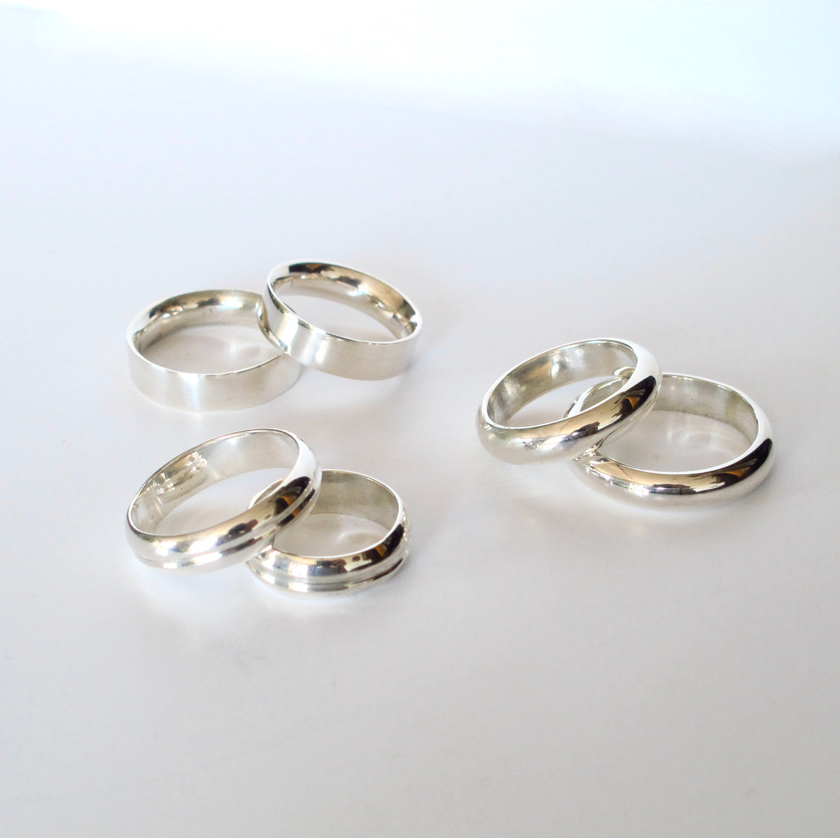Five polished silver rings arranged in two groups on a clean white background.