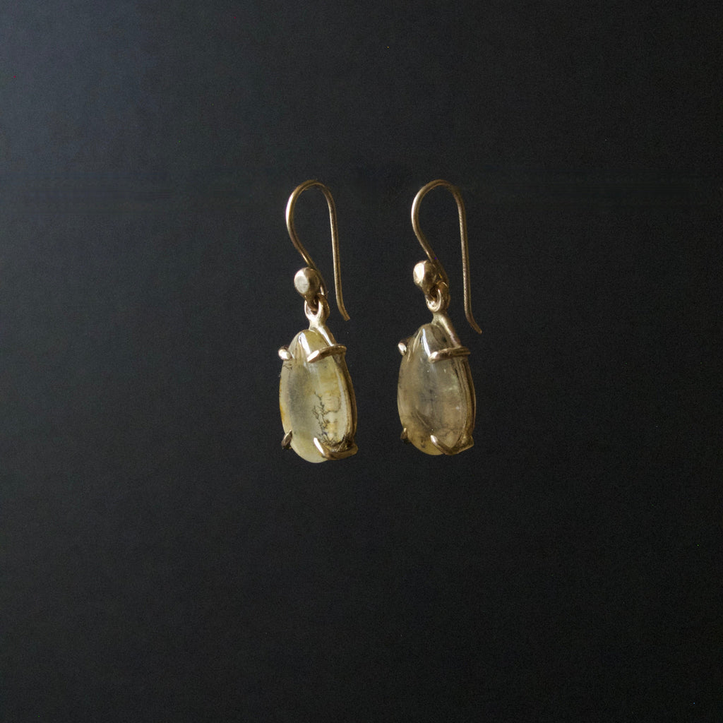 A pair of gold-tone dangle earrings with teardrop-shaped clear gemstones, shown against a solid black background.