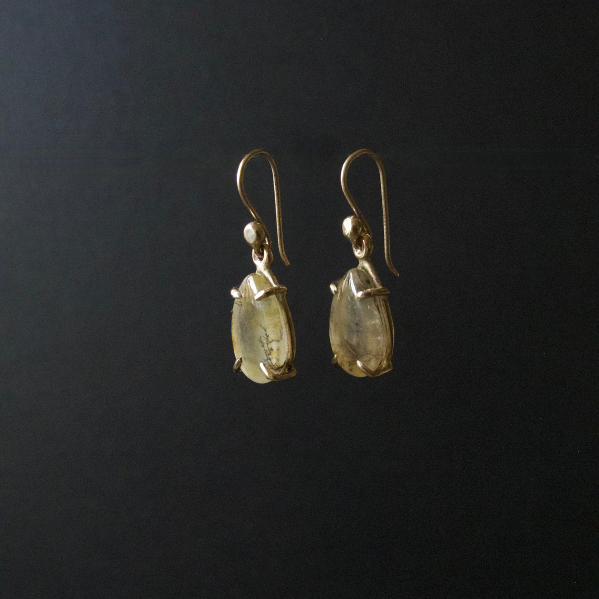 A pair of gold-tone dangle earrings with teardrop-shaped clear gemstones, shown against a solid black background.