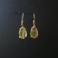 A pair of gold drop earrings with teardrop-shaped clear gemstones containing inclusions, set against a dark black background.