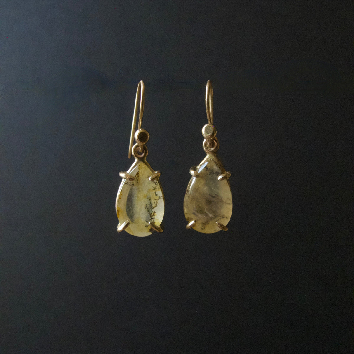 A pair of gold drop earrings with teardrop-shaped clear gemstones containing inclusions, set against a dark black background.