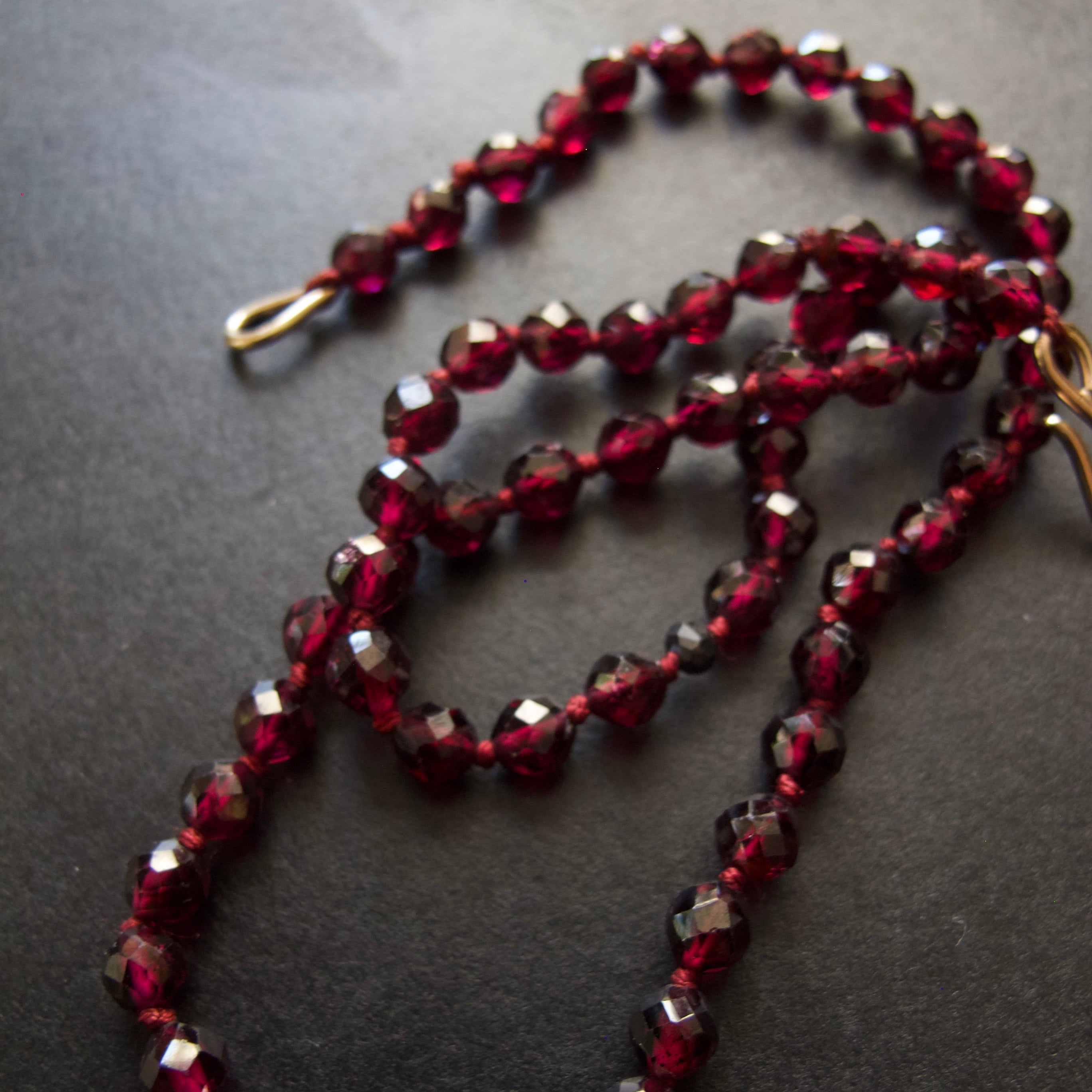 A beaded necklace made of faceted dark red glass beads, arranged in loops on a dark gray textured background.