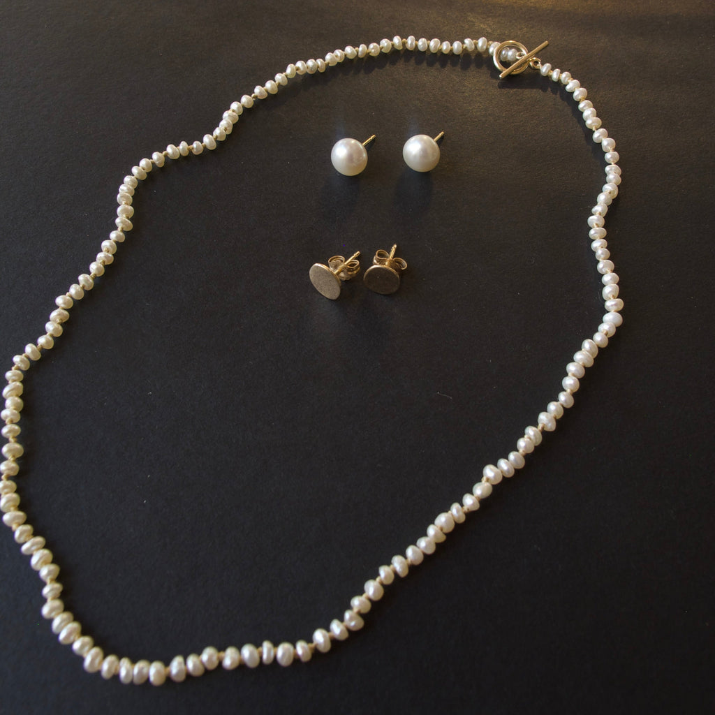 A pearl necklace and matching pearl stud earrings with gold-tone heart stud earrings, arranged on a dark surface.