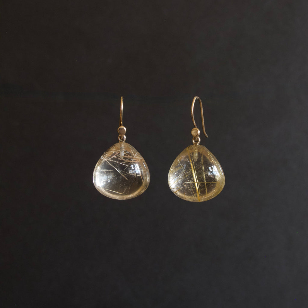 A pair of gold-tone dangle earrings with teardrop-shaped clear resin pendants containing fine gold filaments, shown against a solid black background.