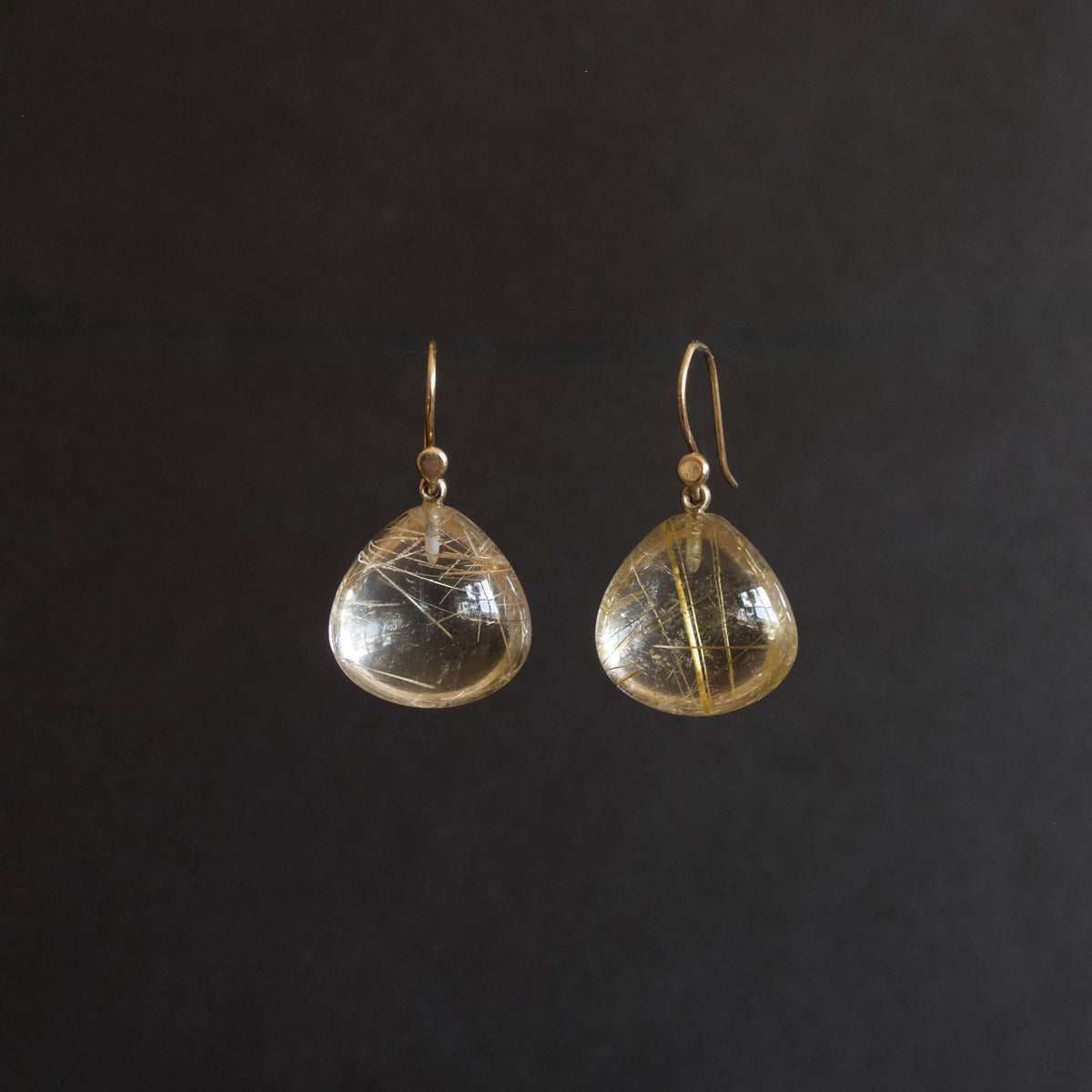 A pair of gold-tone dangle earrings with teardrop-shaped clear resin pendants containing fine gold filaments, shown against a solid black background.