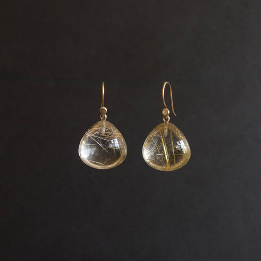 A pair of gold-tone dangle earrings with teardrop-shaped clear resin pendants containing fine gold filaments, shown against a solid black background.