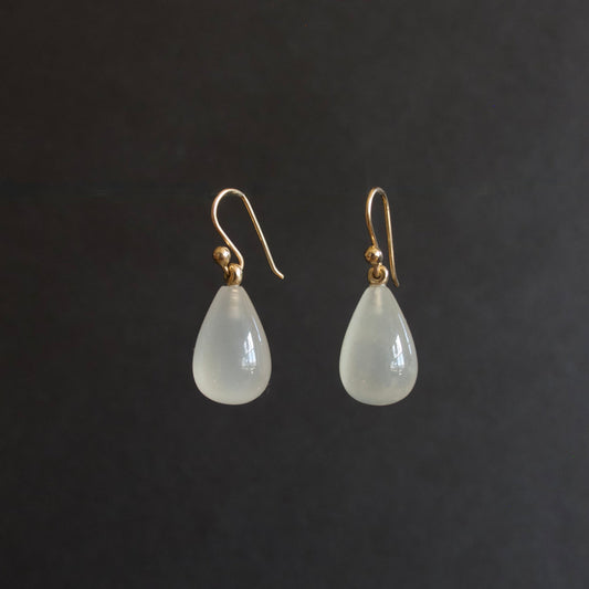 A pair of teardrop-shaped drop earrings with milky white translucent beads and gold fishhook wires, displayed against a dark gray background.