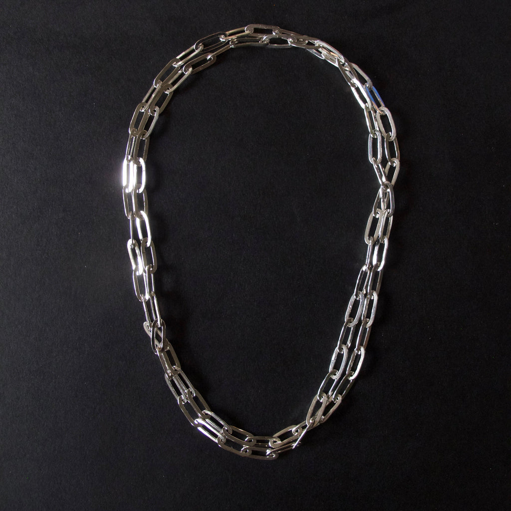 A silver-toned chain necklace with elongated oval links, arranged in a loose loop on a solid black background.