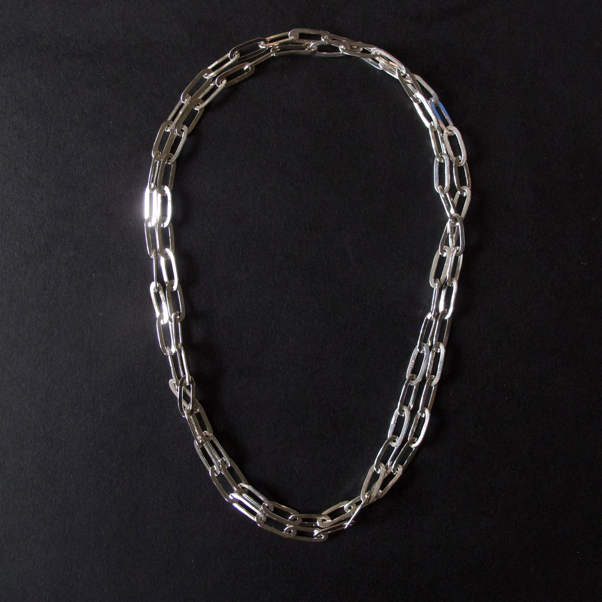 A silver-toned chain necklace with elongated oval links, arranged in a loose loop on a solid black background.