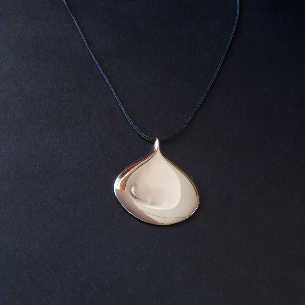 A teardrop-shaped pendant necklace with a polished silver-toned finish, suspended from a dark navy blue cord against a dark textured background.