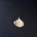 A teardrop-shaped pendant necklace with a polished silver-toned finish, suspended from a dark navy blue cord against a dark textured background.