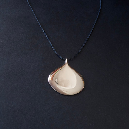 A teardrop-shaped pendant necklace with a polished silver-toned finish, suspended from a dark navy blue cord against a dark textured background.