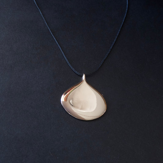 A teardrop-shaped pendant necklace with a polished silver-toned finish, suspended from a dark navy blue cord against a dark textured background.