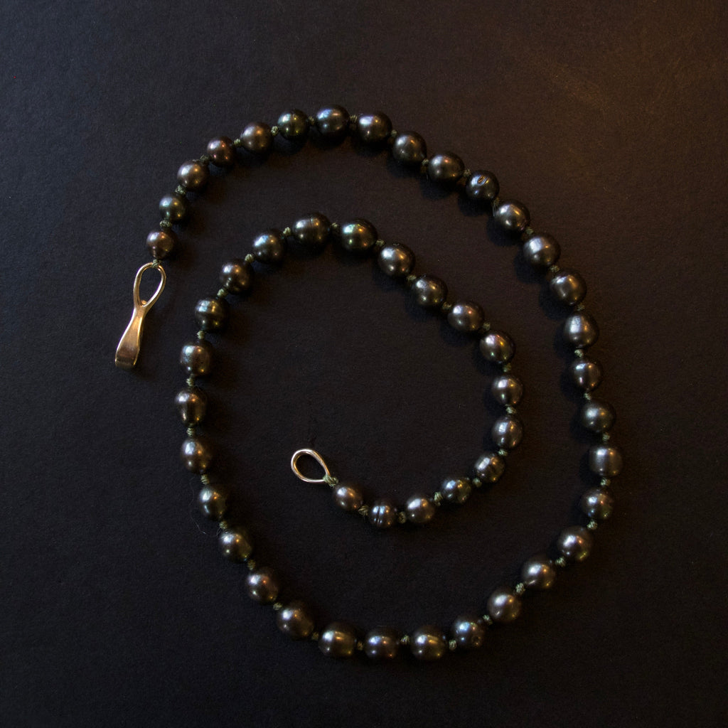 A beaded necklace made of dark, glossy round beads with a small gold-toned clasp, arranged on a dark black background.