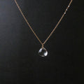 A delicate gold chain necklace with a small clear teardrop-shaped crystal pendant, displayed against a dark black background.