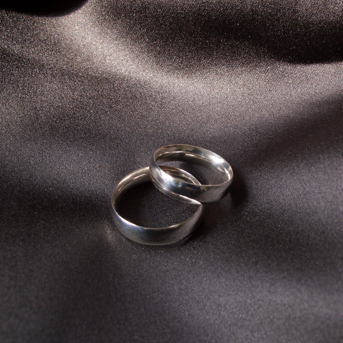 Two polished silver rings interlocked on a dark, draped satin fabric background.