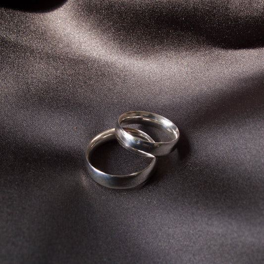 Two polished silver rings interlocked on a dark, draped satin fabric background.