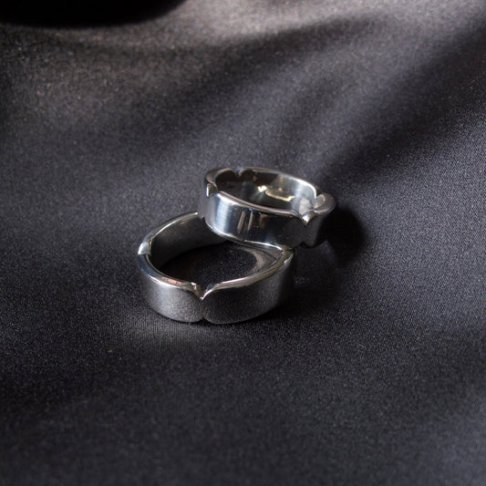 Two silver-toned metal rings with a textured, organic wavy design, resting on a dark, satin-textured surface.